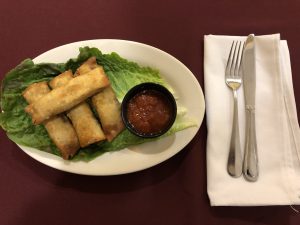 A plate of spring rolls and a fork on a table.